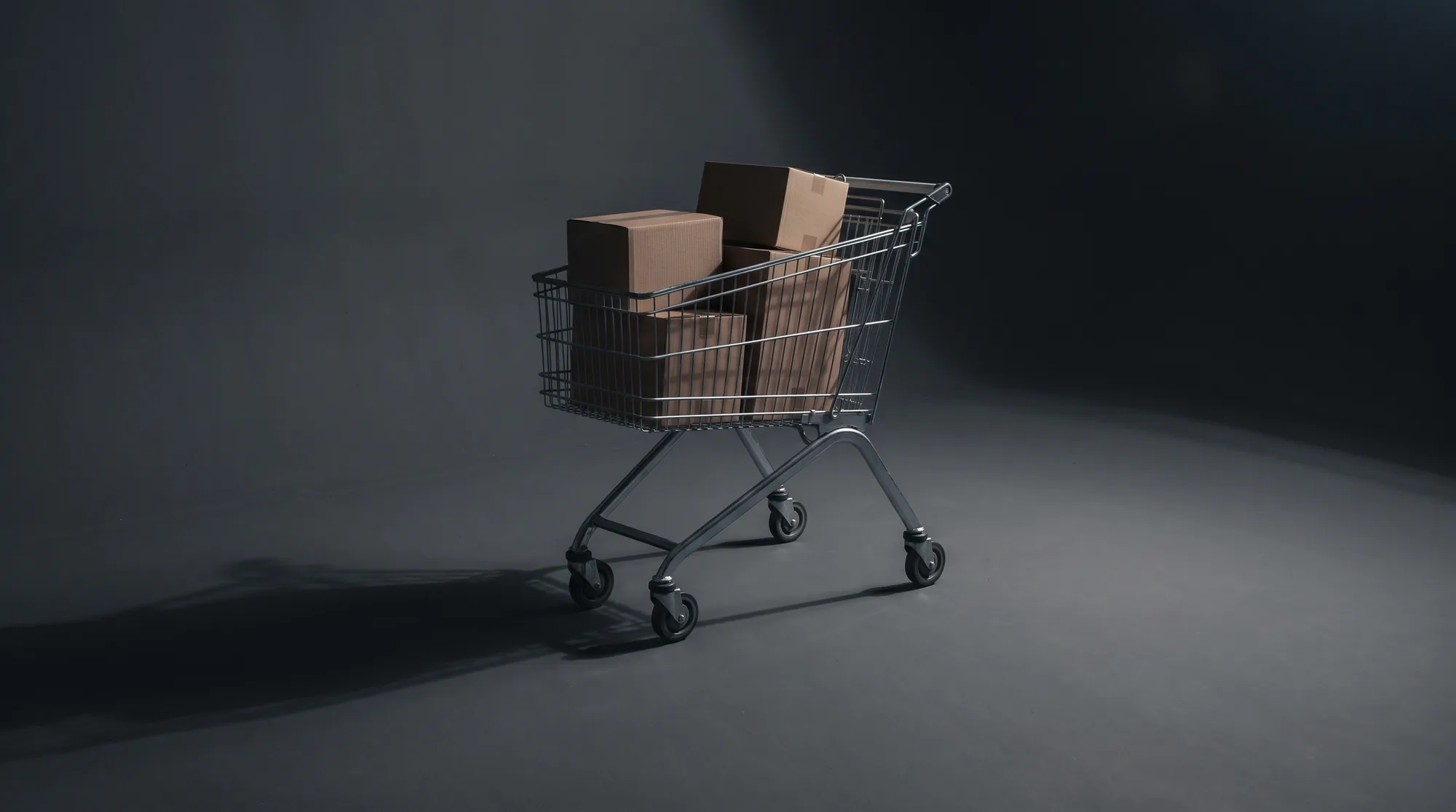 A shopping trolley half filled with plain cardboard boxes, left standing alone on a dark studio floor under a hard light that throws a long shadow.